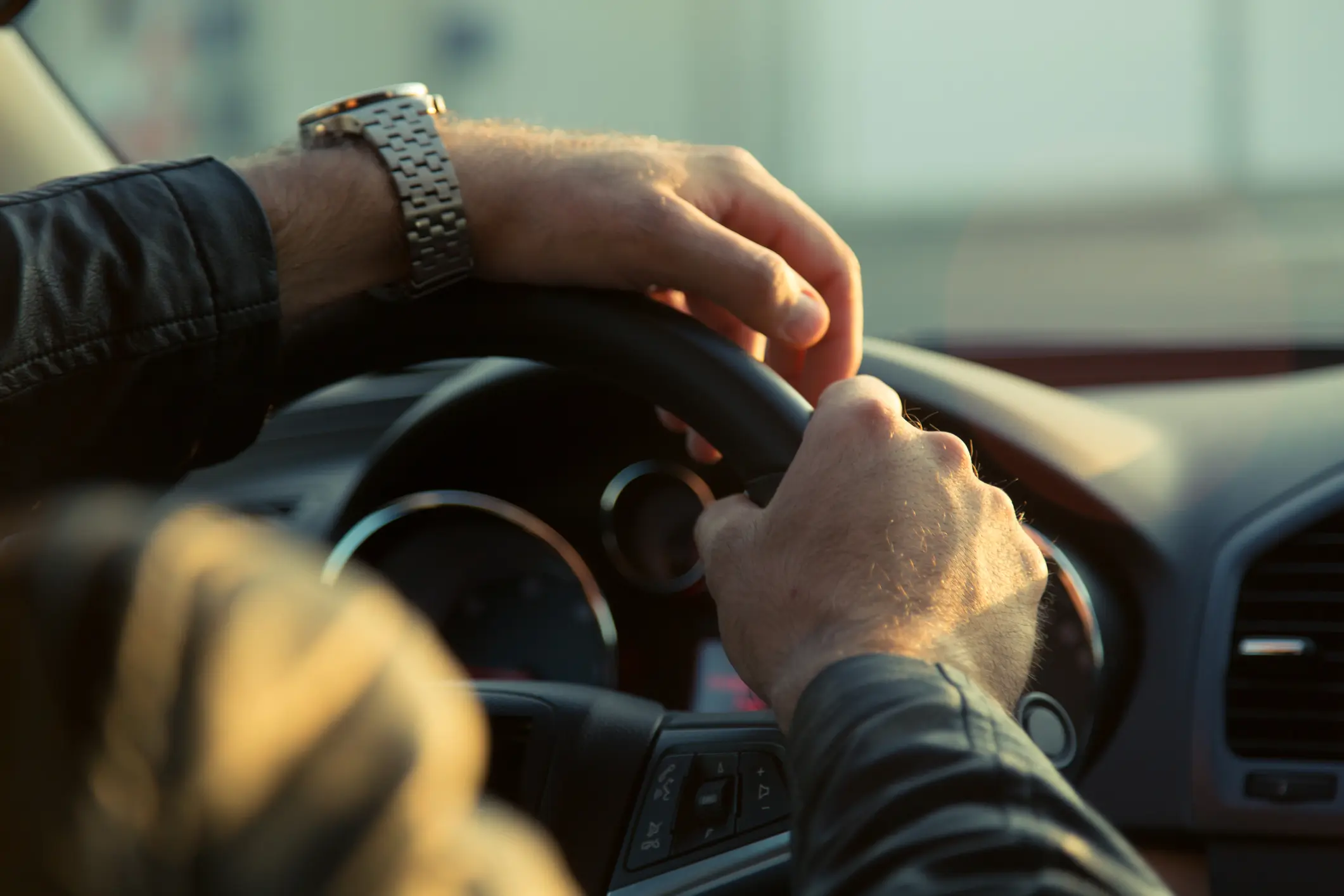 Hands gripping steering wheel, wearing leather jacket.
